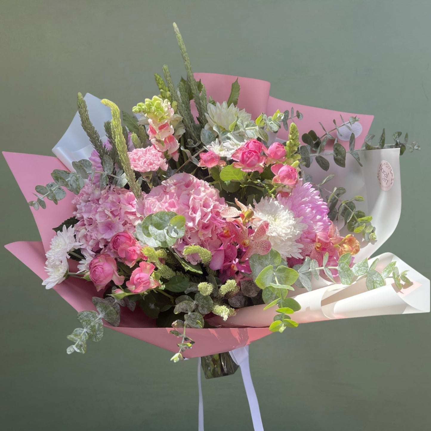 Bouquet of flowers wrapped in pink paper with a white ribbon on a green background