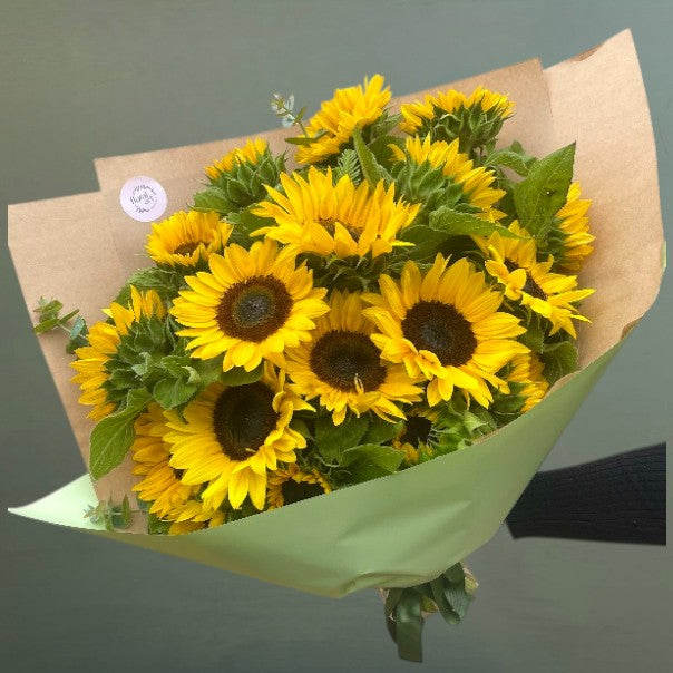 Bouquet of sunflowers wrapped in brown paper with a green bow on a gray background