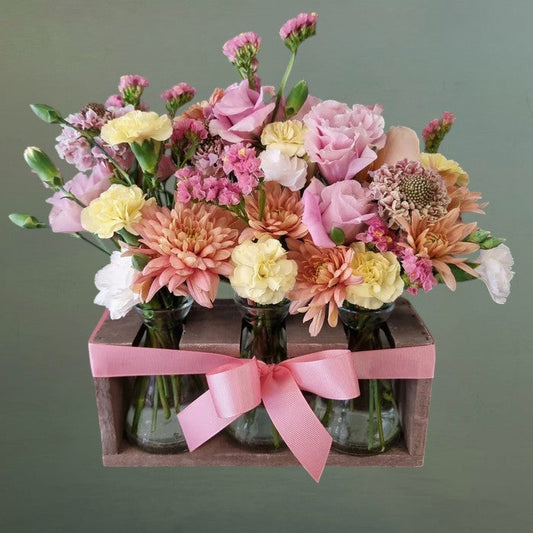 Stand of flowers in small vases with a pink ribbon on a green background