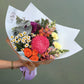 Bouquet of colorful flowers held by a hand with a green background