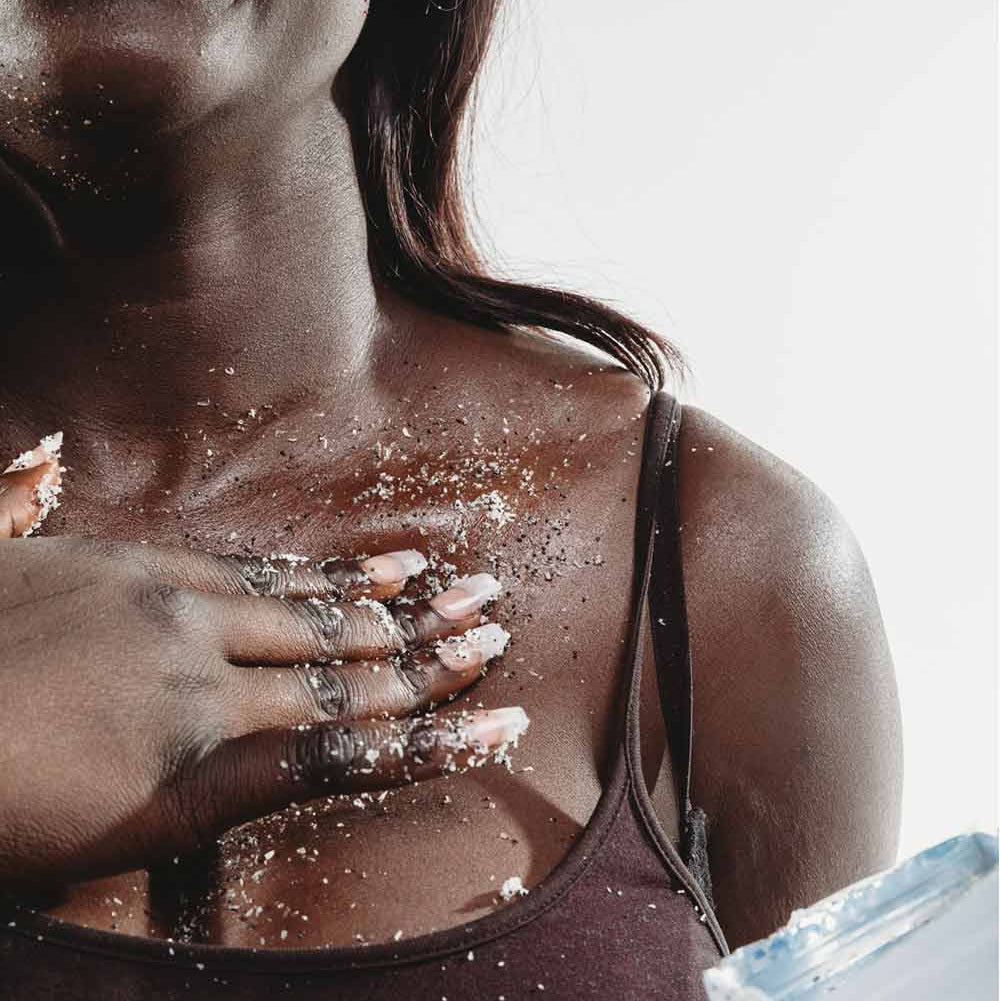 Woman applying scrub product to her skin with a white background