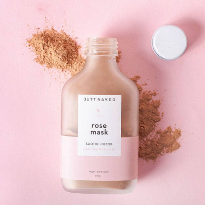 Butt Naked rose mask bottle on a pink background with rose powder around it.
