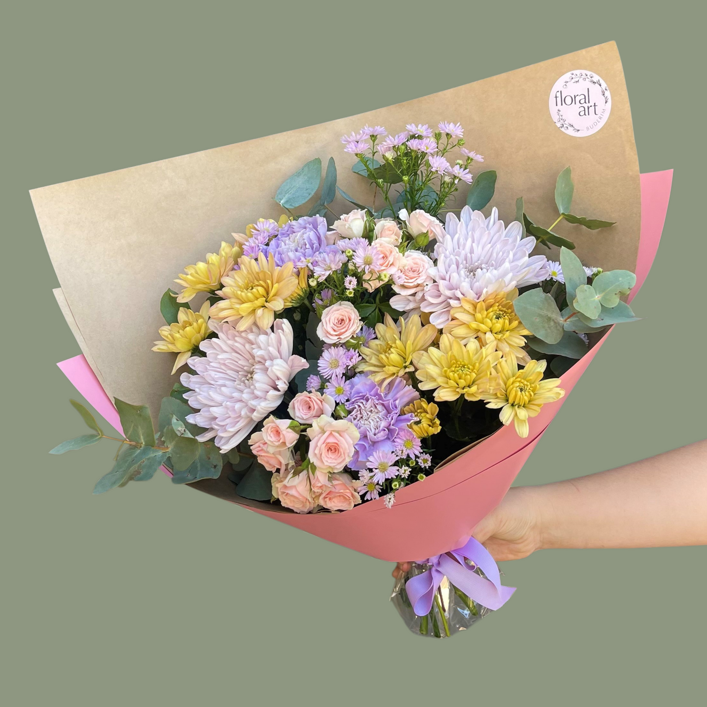 Bouquet of flowers wrapped in brown paper with a pink ribbon, held by a hand on a green background.