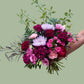 Bouquet of pink, red, and white flowers held by a hand against a light green background