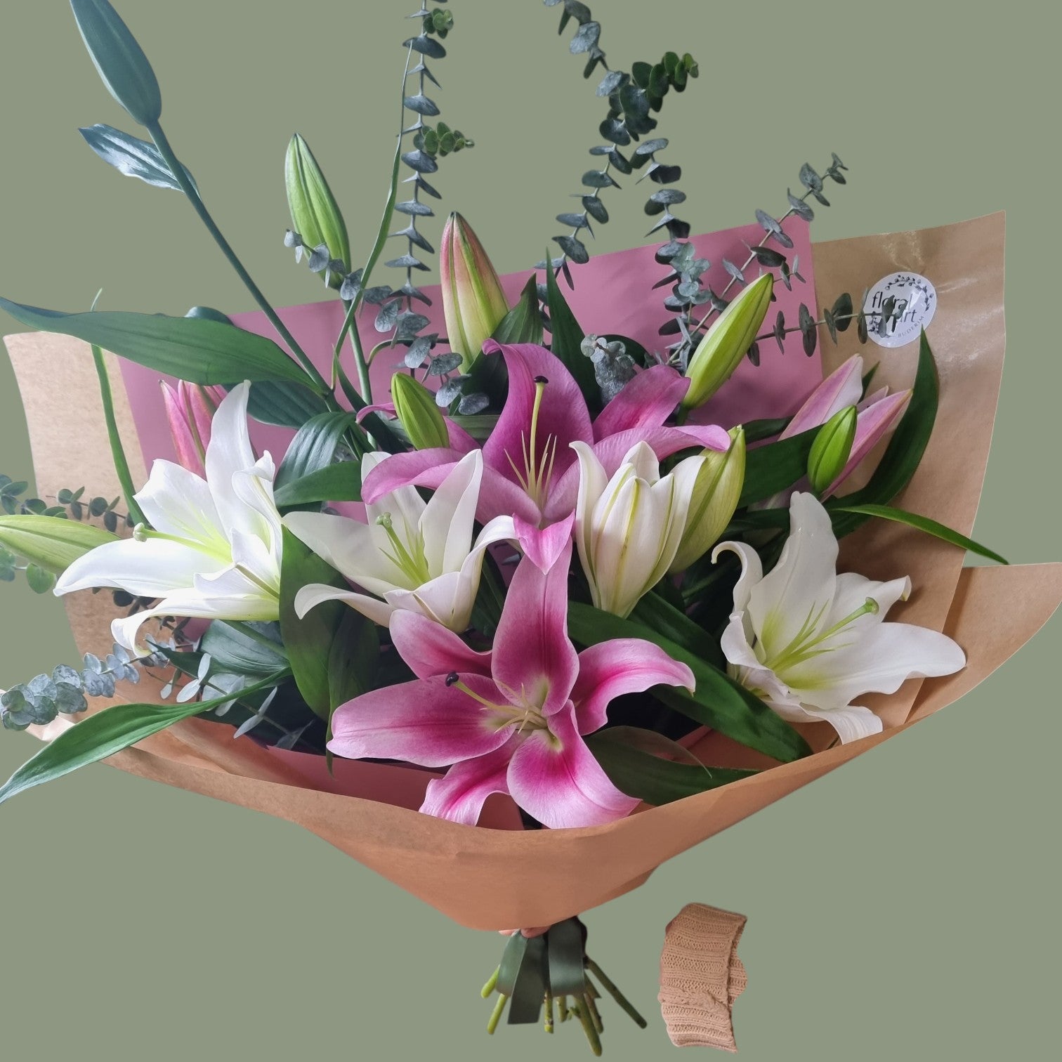 Bouquet of pink and white lilies with greenery in brown paper wrapping on a light green background