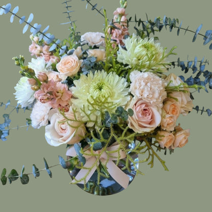 peach coloured flowers with sage foliage in a clear vase