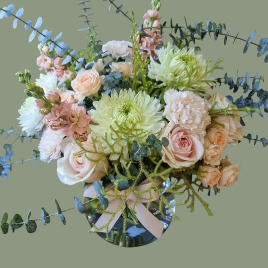 peach coloured flowers with sage foliage in a clear vase