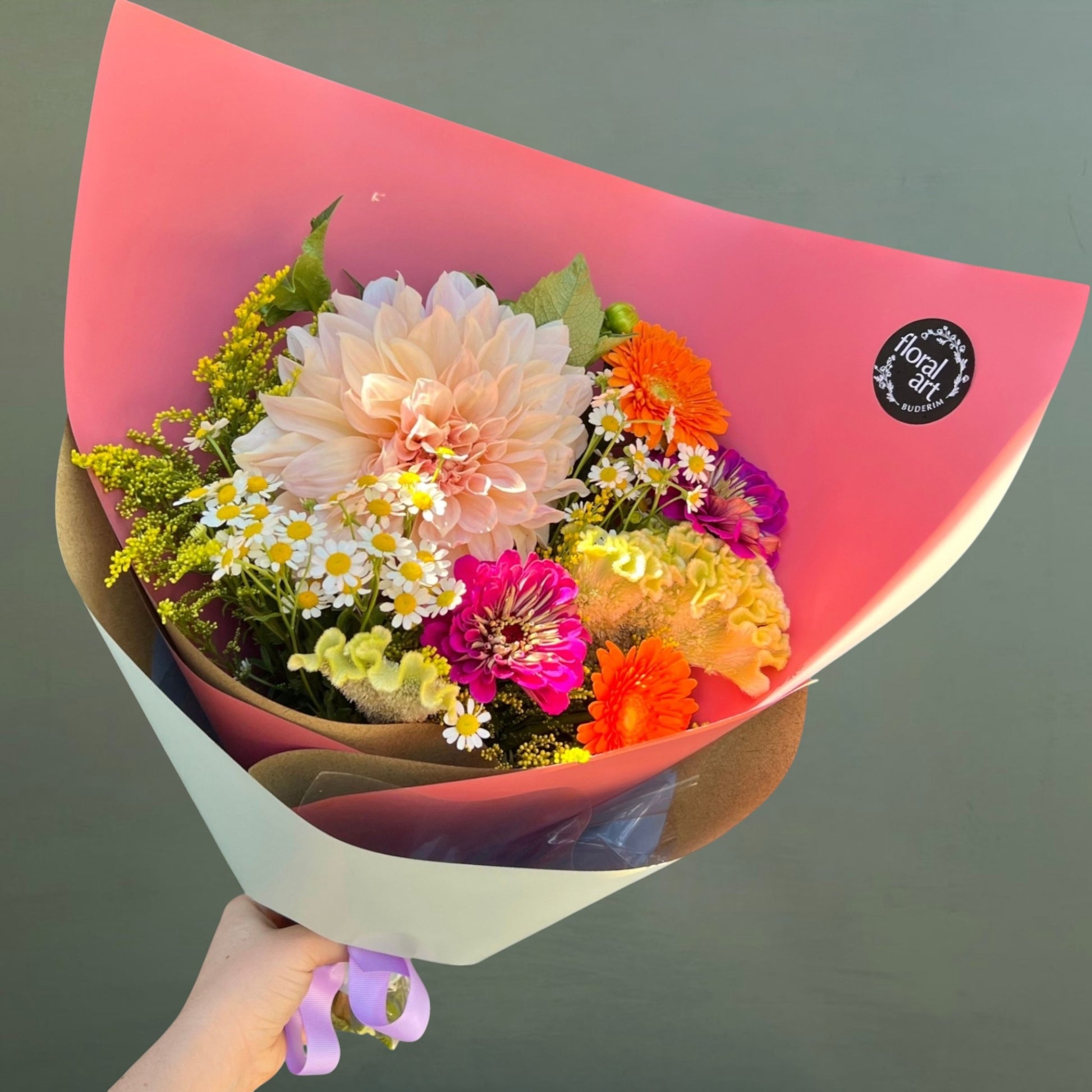 Bouquet of colorful flowers wrapped in pink paper with a visible brand label.