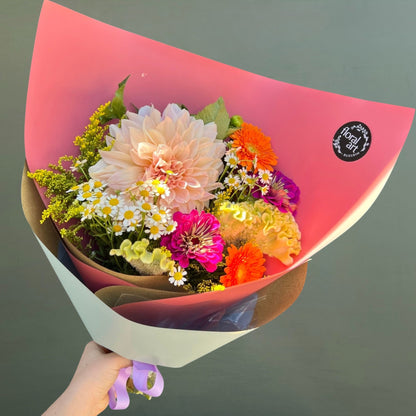 Bouquet of colorful flowers wrapped in pink paper with a visible brand label.