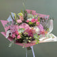 Bouquet of flowers wrapped in pink paper with a white ribbon on a green background