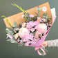 Bouquet of pink flowers wrapped in brown paper with a visible brand logo on a dark background