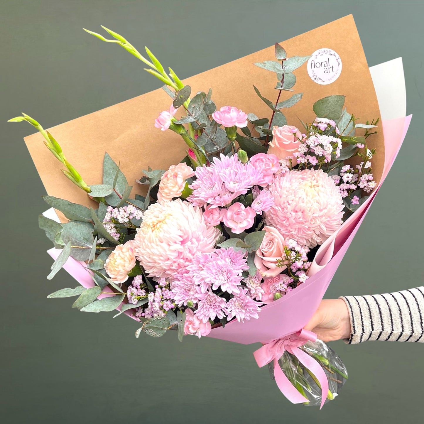 Bouquet of pink flowers wrapped in brown paper with a visible brand logo on a dark background