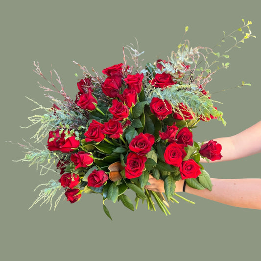 Bouquet of red roses held by a person against a plain background