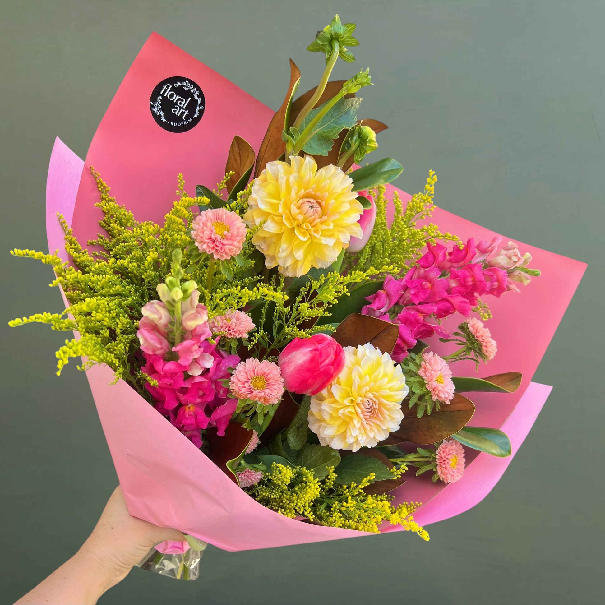 Bouquet of flowers wrapped in pink paper with a visible brand logo on a dark background