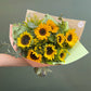 Bouquet of sunflowers wrapped in brown paper with a green leaf detail, held against a dark background