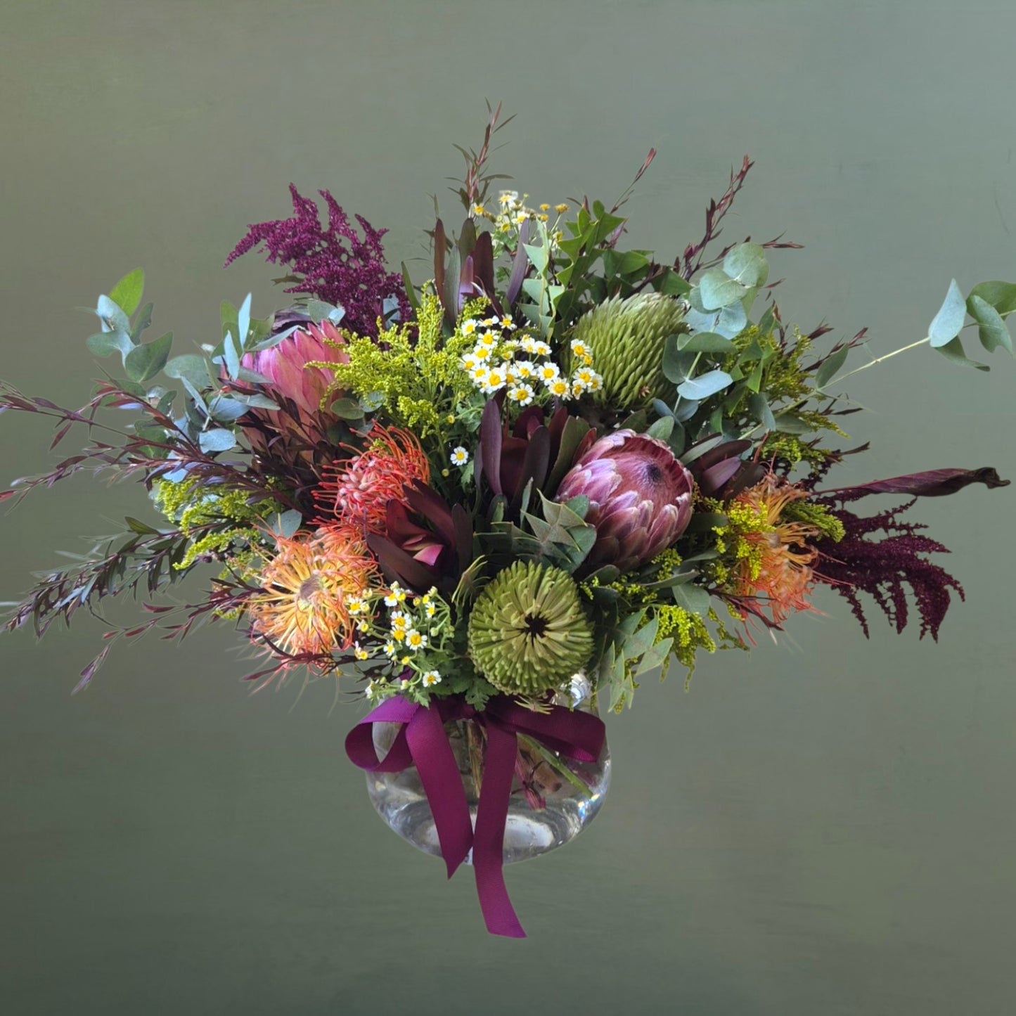 Colorful bouquet of Native flowers with a clear vase on a green background