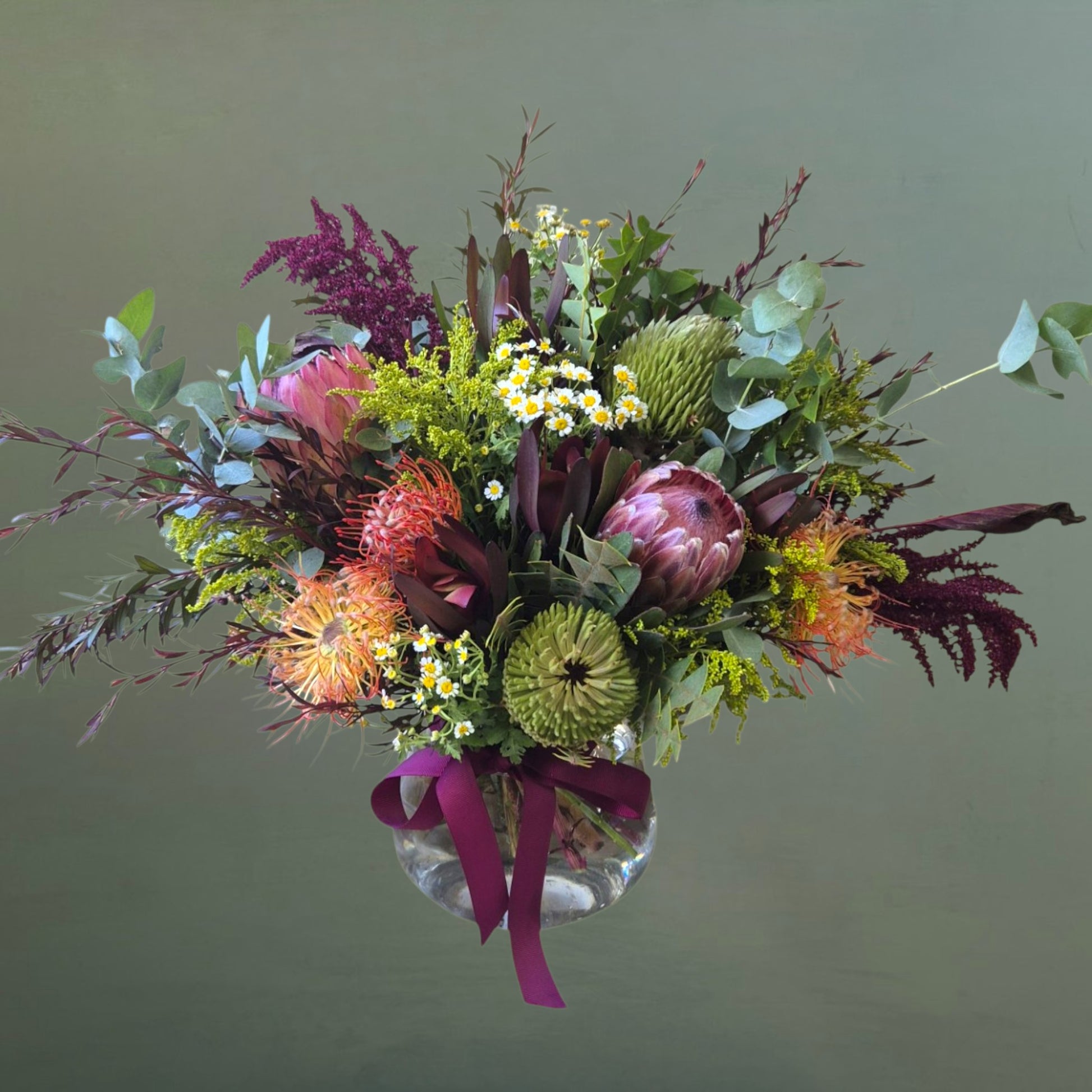 Colorful bouquet of Native flowers with a clear vase on a green background