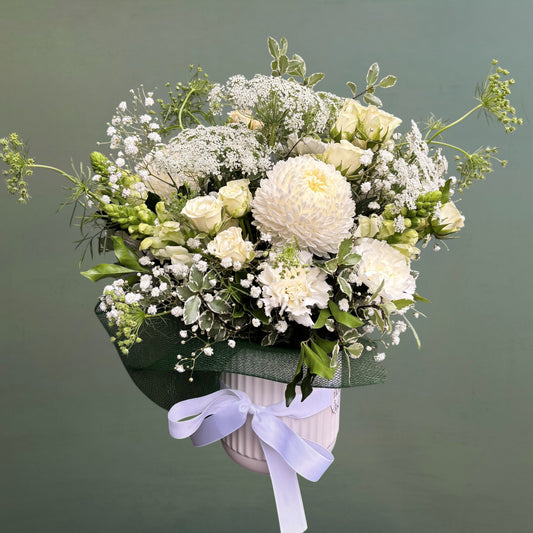 Ceramic vase of white and green flowers with a white ribbon on a dark background