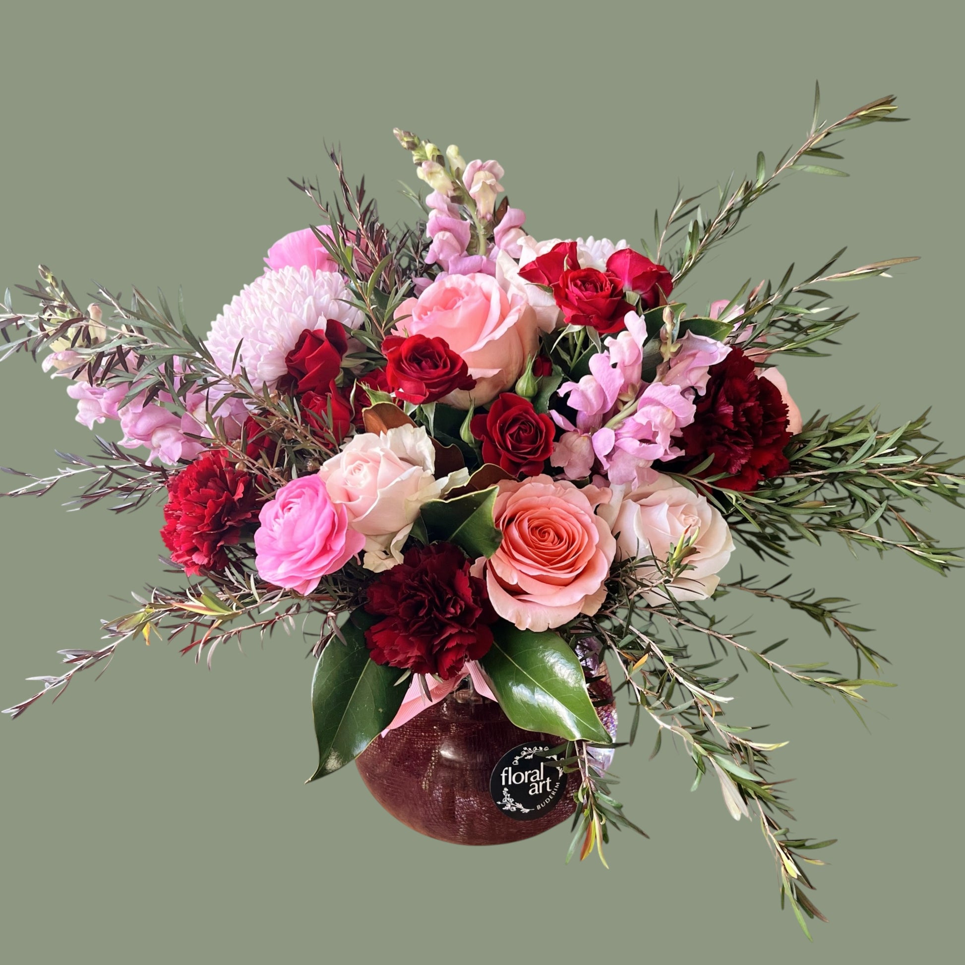 Bouquet of red and pink flowers with greenery in a clear vase on a green background