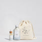 Skincare products including a bottle, dropper, and drawstring bag on a light gray background